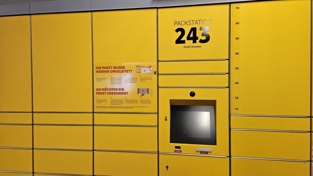 Gelbe DHL Packstation am Bahnhof Mitte Dresden, unter einer Überdachung, bereit zur Paketabholung.